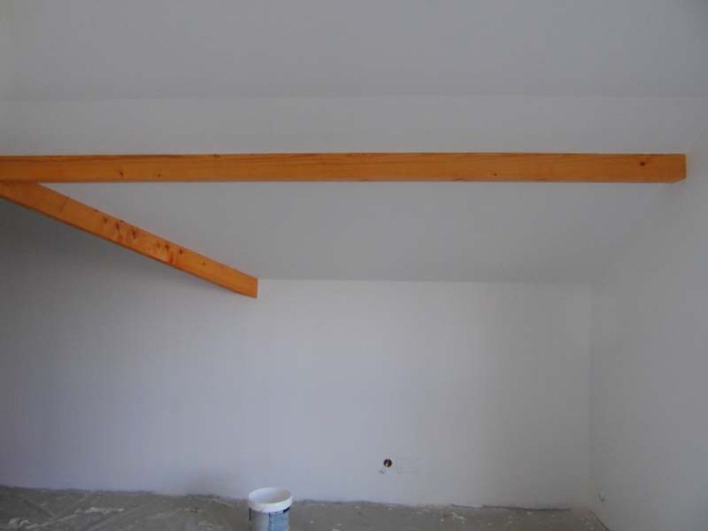 Application de peinture blanche sur mur sous comble avec poutres en bois apparentes – Travaux de peinture intérieure AK Rénovation dans le Pays de Gex